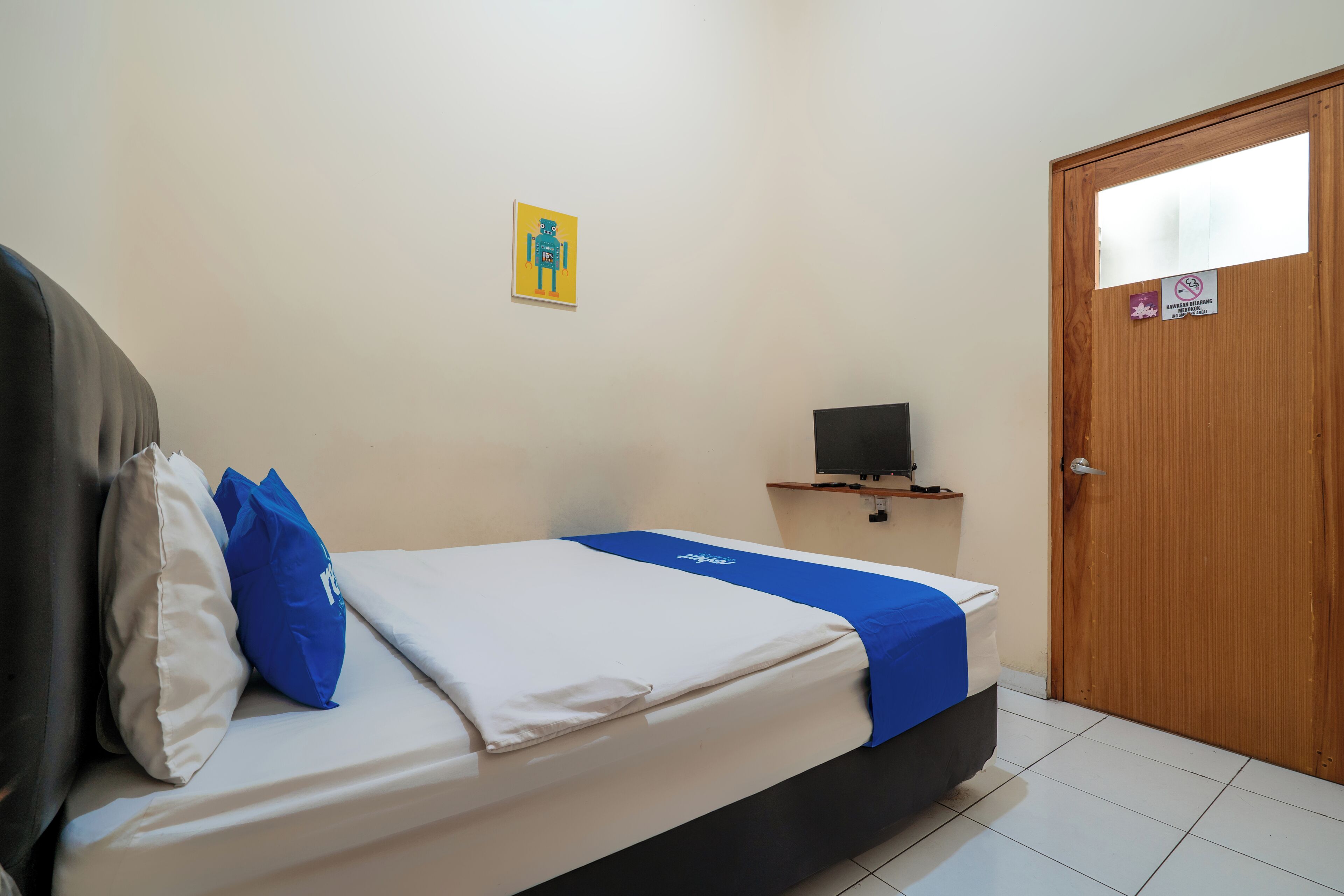 Habitación de hotel con una cama, un televisor sobre un soporte, una puerta de madera y una obra de arte colgada en la pared.