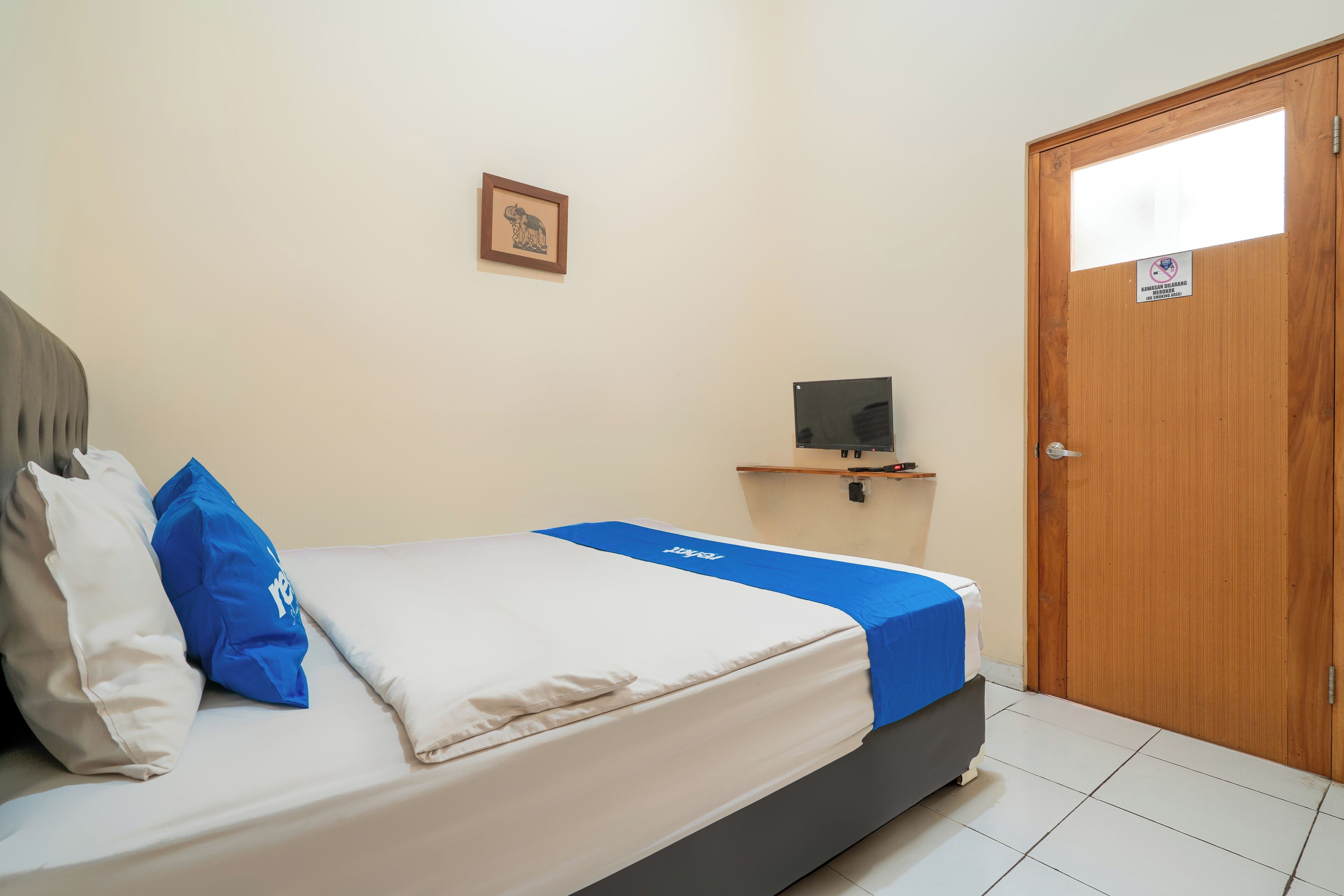 Een slaapkamer met een bed, kussens, een televisie op een standaard en een houten deur.