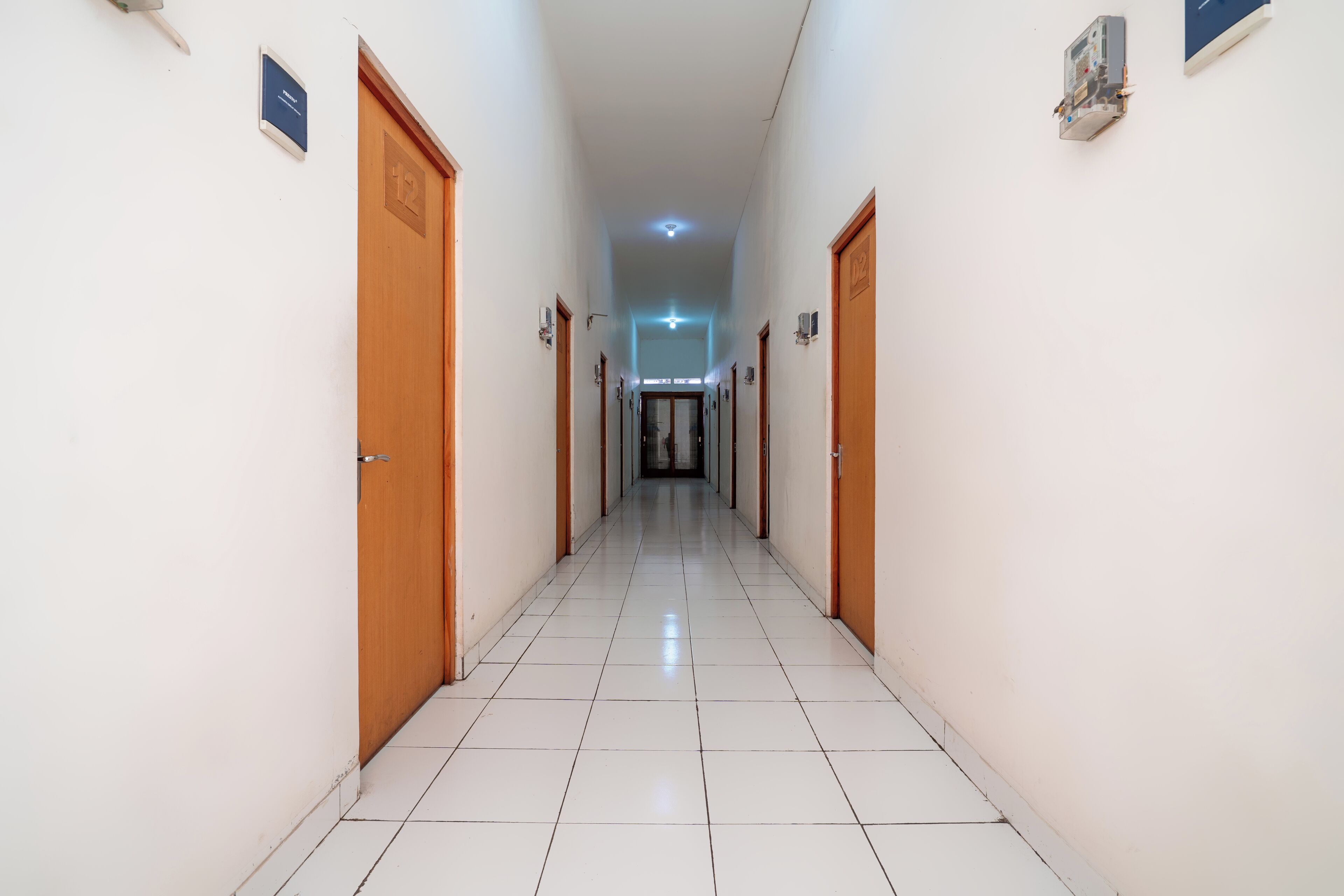 A long, narrow hallway with white tiled floors and wooden doors on both sides.