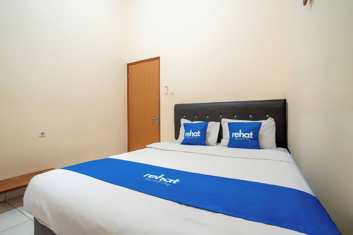 A hotel room with a bed, a wooden door, and a blue bedspread with the hotel name.