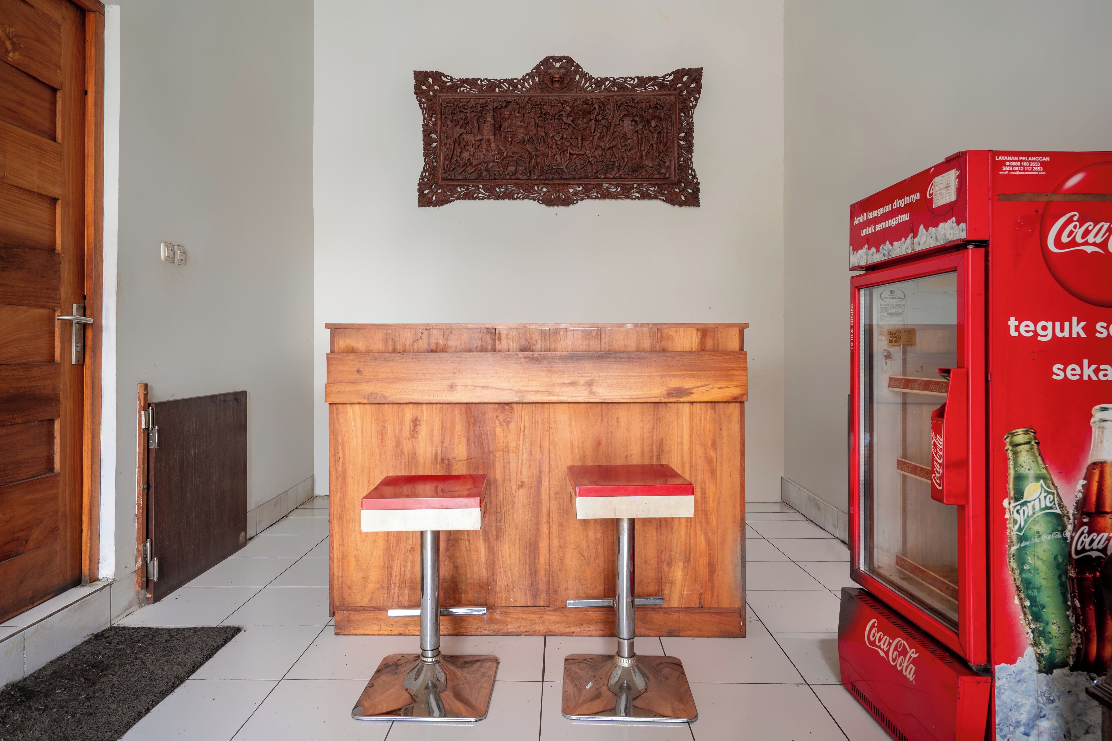 A bar area with two stools, a wooden counter, a decorative wall piece, and a Coca-Cola refrigerator.
