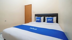 Ein ordentlich bezogenes Bett mit blauer Bettdecke und Kissen, eine Holztür und eine weiße Wand.