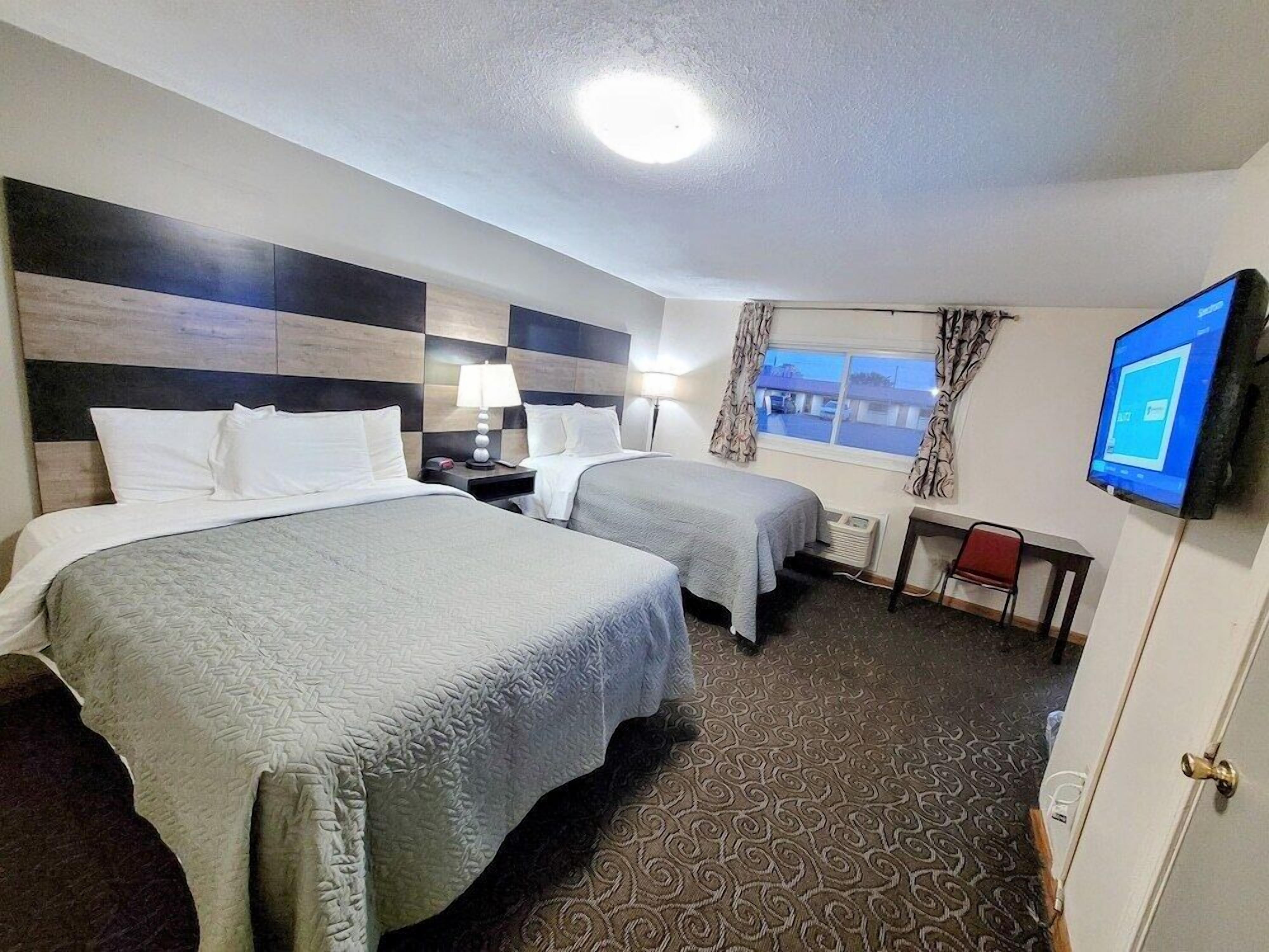 A hotel room with two beds, a desk, a chair, a TV, and a window with curtains.
