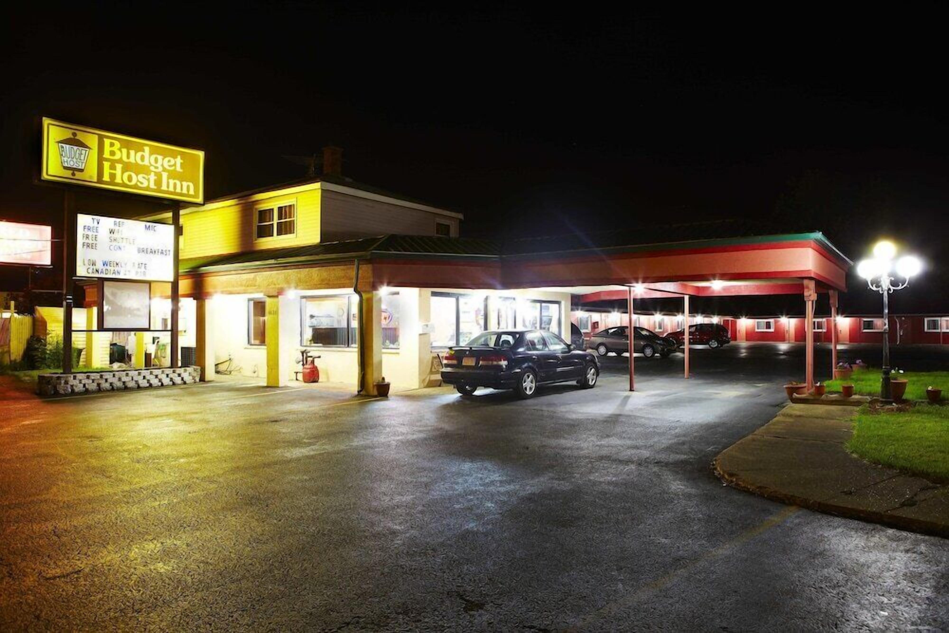 A Budget Host Inn with a well-lit entrance, a covered parking area, and a visible car in the lot.