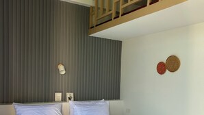 Un lit bien fait, avec une tête de lit en bois, un mur à rayures grises et deux interrupteurs d’éclairage fixés au mur.