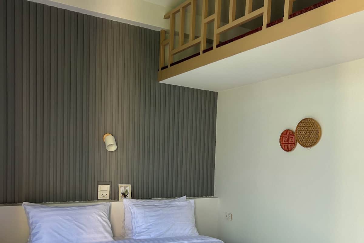 A neatly made bed with a wooden headboard, a grey striped wall, and two wall-mounted light switches.