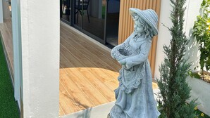 Une statue d’une femme tenant une branche, une porte en bois avec une inscription et un petit arbre.