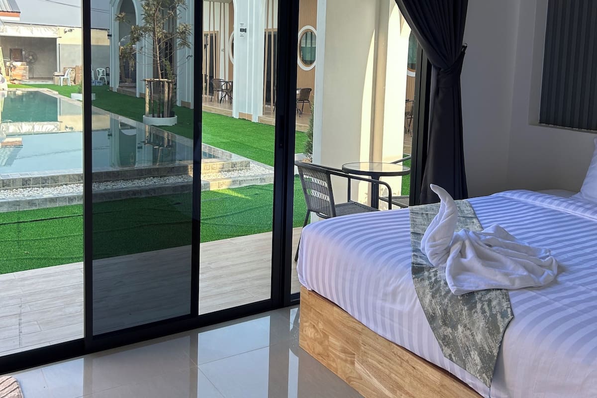 A hotel room with a large sliding glass door leading to a pool and garden area.