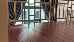 Une terrasse en bois offrant une vue sur un bâtiment, visible à travers une fenêtre ornée de rideaux noirs.