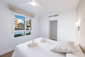 A hotel room with a bed, a ceiling fan, a window with a view of buildings, and a door. - Luxury Pool View Isea 1111 (Torrox Costa)