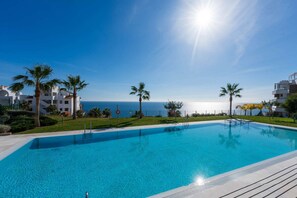 A clear blue pool with a view of the sea, surrounded by palm trees and modern buildings. - Luxury Pool View Isea 1111 (Torrox Costa)