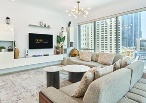 Ein modernes Wohnzimmer mit einer großen Couch, zwei runden Couchtischen, einem Flachbildfernseher und Blick auf die Stadt.