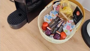 Una cafetera con una cesta de bocadillos variados y un cuenco pequeño de fruta sobre una mesa de madera.