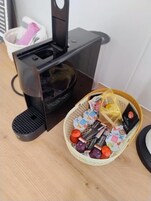 Una cafetera con una cesta de bocadillos variados y un cuenco pequeño de fruta sobre una mesa de madera.