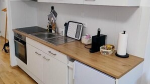 Una cocina compacta con armarios blancos, encimera de madera, horno integrado y un refrigerador pequeño.