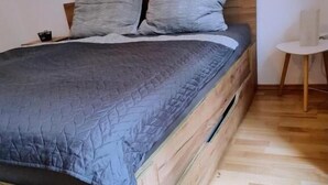 Una cama con estructura de madera y colcha gris.