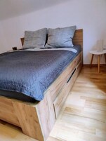 Una cama con estructura de madera y colcha gris.