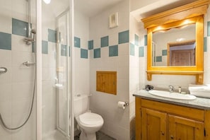 Une salle de bain avec une douche à parois de verre, des toilettes, un meuble en bois avec un lavabo et un miroir avec un cadre en bois.
