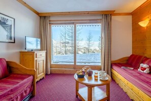 Um quarto aconchegante com uma cama, um armário de madeira, uma mesa com itens de café da manhã e uma janela com vista para a neve.