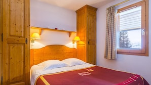 Una cama de madera con dos lámparas de noche, una ventana con cortinas y un armario de madera.