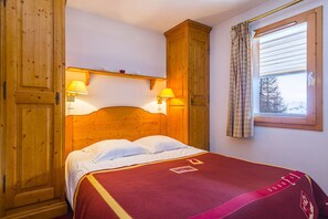 Uma cama de madeira com duas luminárias de cabeceira, uma janela com cortinas e um guarda-roupa de madeira.