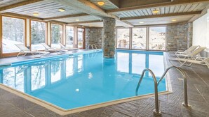 Una piscina interior con vistas despejadas al exterior, pilares de piedra y vigas de madera en el techo.