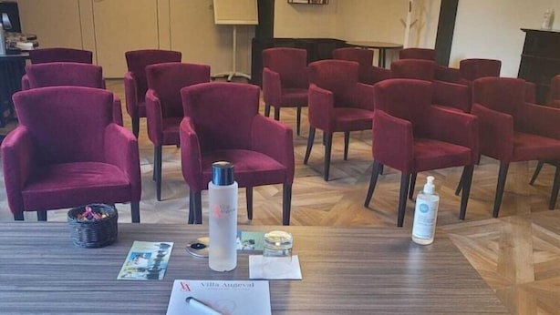 A conference room with multiple red chairs arranged around a central table, equipped with a bottle of hand sanitizer and a notepad. - Laugeval (Deauville)