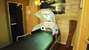 A treatment room with a massage table, a wall-mounted light, and a broom. - Laugeval (Deauville)