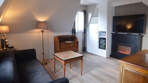 A cozy living room with a sofa, a table, a lamp, a fireplace, and a television. - Laugeval (Deauville)