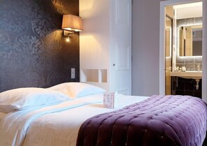 A hotel room with a bed, a nightstand, a lamp, a bathroom with a mirror, and a door. - Laugeval (Deauville)