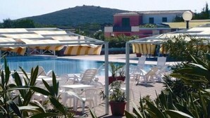 Zona de piscina amb gandules i ombrel·les, envoltada de plantes en testos i una muntanya al fons.