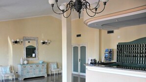 Una zona d'estació amb un paviment de marbre, un tocador blau cel amb mirall, una taula d'informació verda i un penjallum.