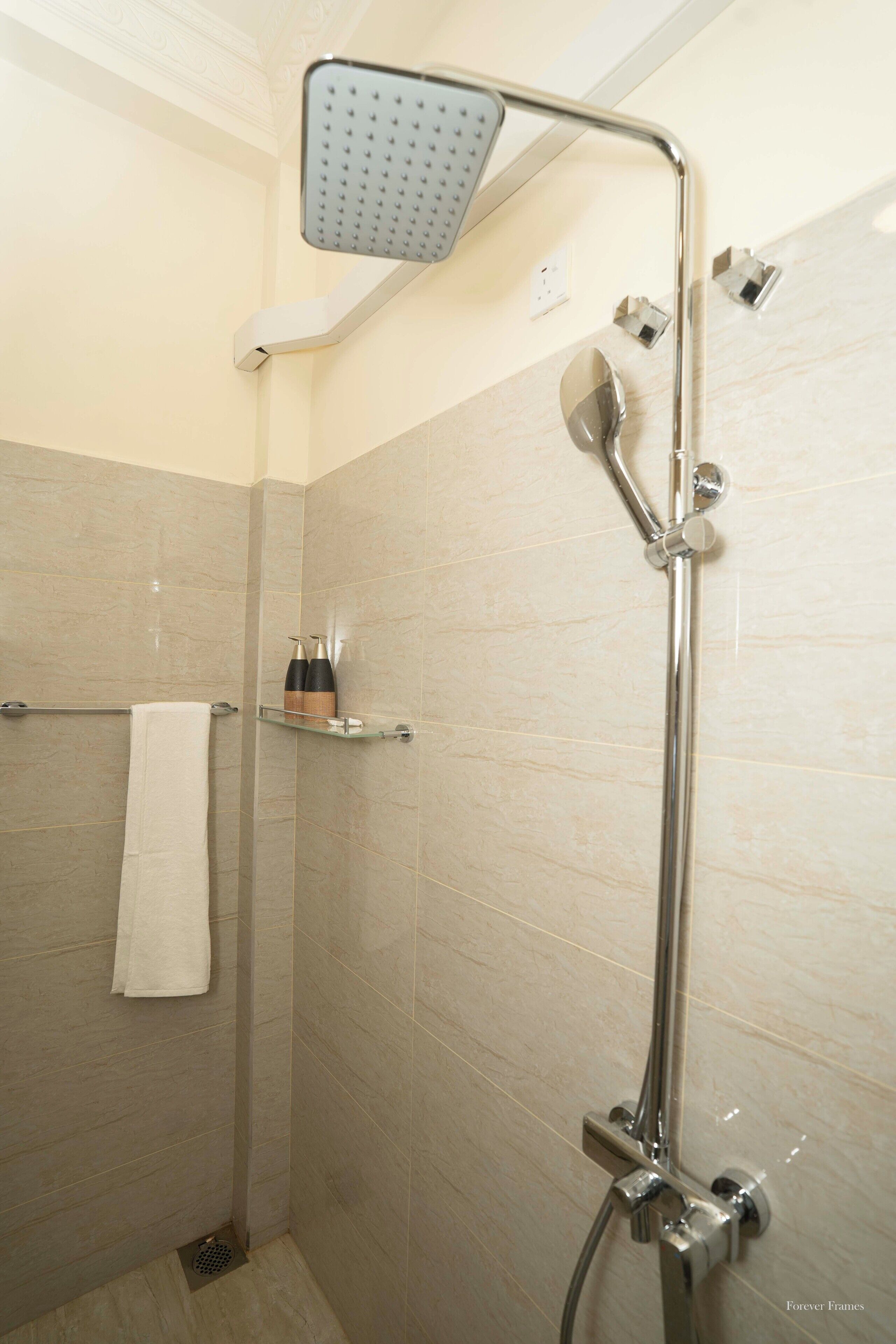 A shower with a handheld showerhead, a towel rack, and a shelf with toiletries.