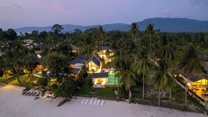 Ein Resort mit mehreren Gebäuden, einem Schwimmbad und einer Strandbucht mit Liegestühlen.