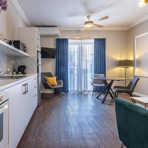 A modern kitchen with a built-in microwave, a sink, and a coffee machine. There is a dining area with a table and chairs, and a ceiling fan. - Park Lane (St. Paul's Bay)