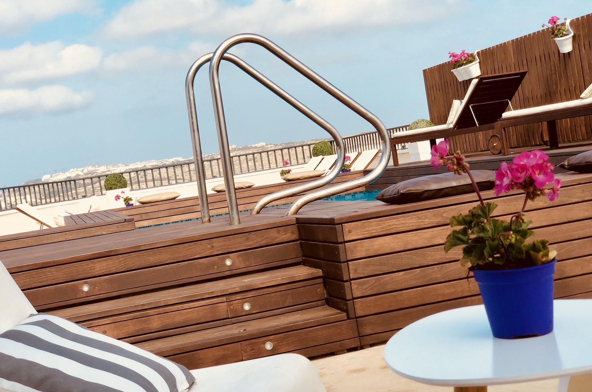 En træterrasse med pool, liggestole og et bord med en potteplante.