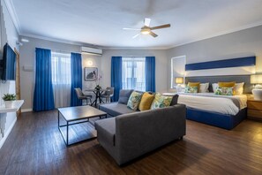 A modern hotel room with a sofa, a bed, a desk, and a ceiling fan. - Park Lane (St. Paul's Bay)