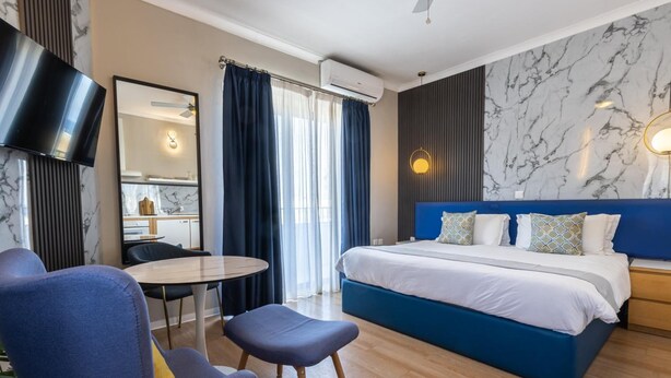 A modern hotel room with a large bed, a desk with a chair, a round table, and a TV. - Park Lane (St. Paul's Bay)