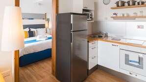 A compact kitchen with a refrigerator, microwave, and oven, a small sink, and wooden shelves above the counter. - Park Lane (St. Paul's Bay)