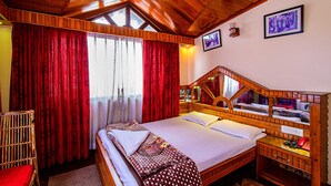 Ein Schlafzimmer mit Holzbettrahmen, einem großen Bett, roten Vorhängen und einem hölzernen Kopfende mit Spiegel.