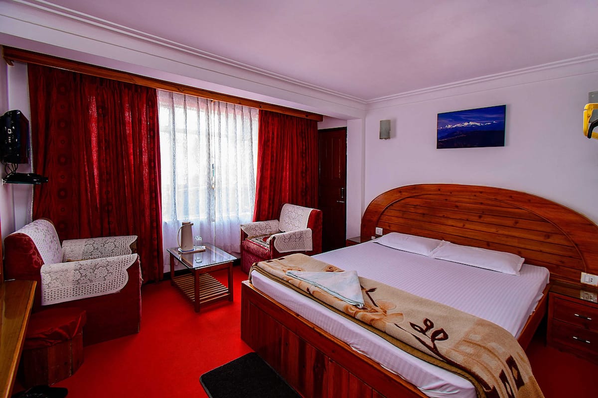 A hotel room with a wooden bed, a red sofa, a small table, and a chair.