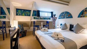 A hotel room with a bed, two chairs, a desk, and artwork on the walls.