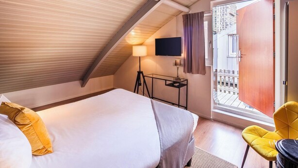 A hotel room with a bed, a desk with a lamp, a TV, and a balcony door.