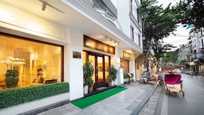 L’entrée d’un hôtel, avec un tapis vert, des plantes en pot et une enseigne au-dessus de la porte.