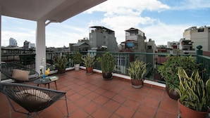 Une terrasse sur le toit agrémentée de plantes en pot, de mobilier d’extérieur et offrant une vue sur le paysage urbain.