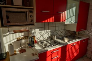 Une cuisine équipée d’un four à micro-ondes, d’une cuisinière à gaz et de meubles de rangement rouges.
