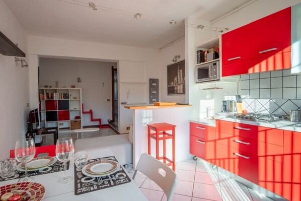 Une cuisine moderne avec des meubles rouges, un coin repas avec une table dressée pour deux personnes, et un escalier menant à un espace de vie.