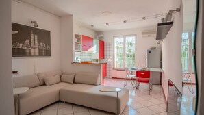 Een moderne woonkamer met een hoekbank, een eethoek met rode stoelen en een keuken met witte kasten.