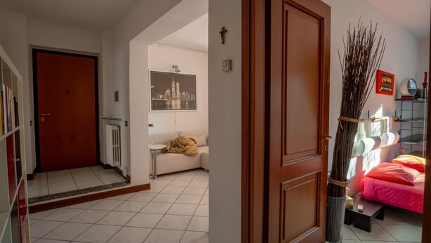 Een hotelkamer met een bed, nachtkastje, raam met uitzicht, deur en gang naar een andere kamer.