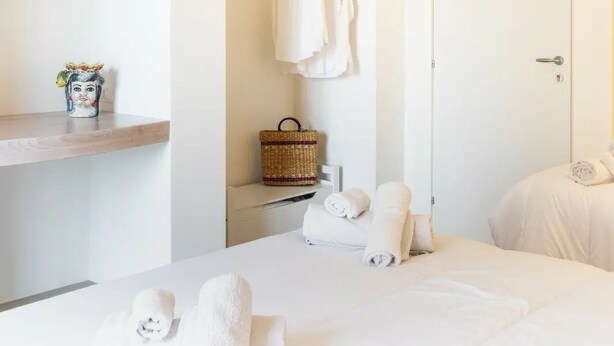 A minimalist hotel room with a bed, a small shelf with a decorative item, a hanging rack with towels, and a door. - Bed&Breakfast Anna's Dream a 500m dal centro storico e 1,2 km dal mare di Avola (Avola)